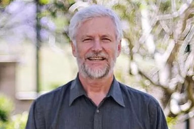 Grey-haired man with grey beard wearing black collared shirt