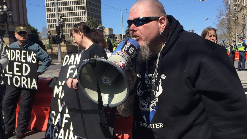 A man wearing a Soldiers of Odin jumper speaks into a megaphone at a rally outside Victoria's Parliament