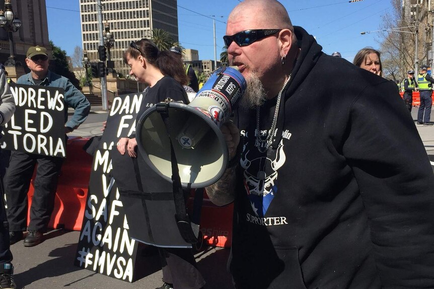 A man wearing a Soldiers of Odin jumper speaks into a megaphone at a rally outside Victoria's Parliament