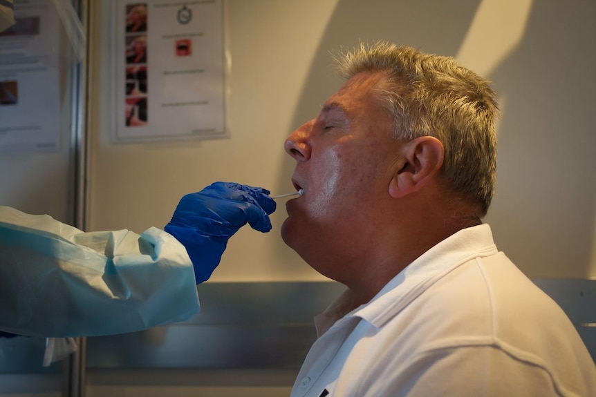 A man with his mouth open as he undergoes a swab test of his throat for coronavirus.