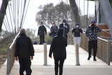 Unidentifiable people wearing masks while walking on a footbridge.