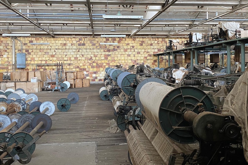Textile machines and materials gather dust inside a decommissioned factory.