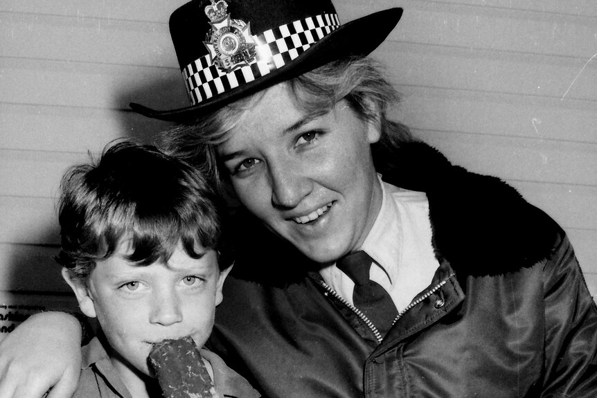 A black and white photo of ya oung Katarina Carroll, in uniform, alongside a child eating ice cream.