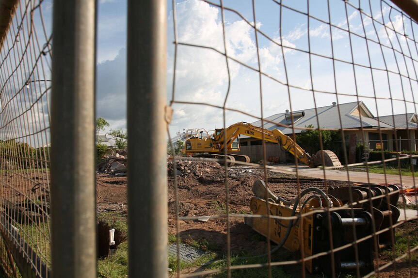 A fenced off construction site containing a bulldozer and a demolished house.