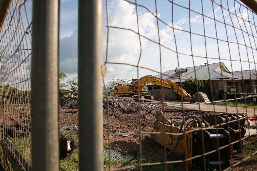 A fenced off construction site containing a bulldozer and a demolished house.