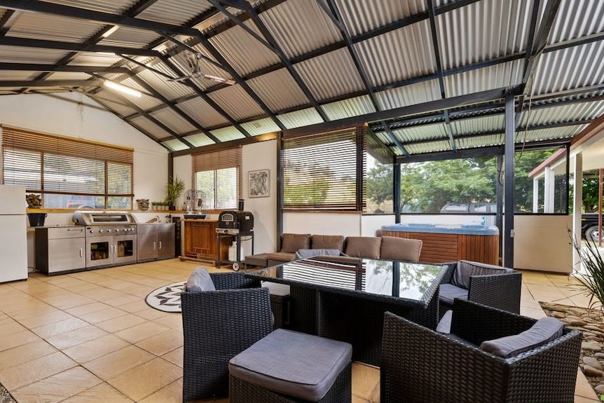 A high-rooved outdoor living space with a tiled floor and barbeque.