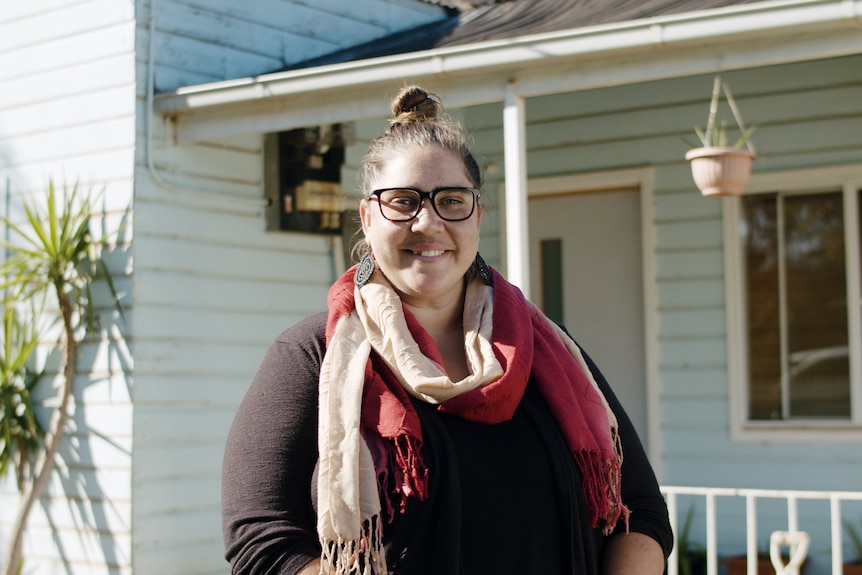 A young Indigenous woman smiling out the front of a home