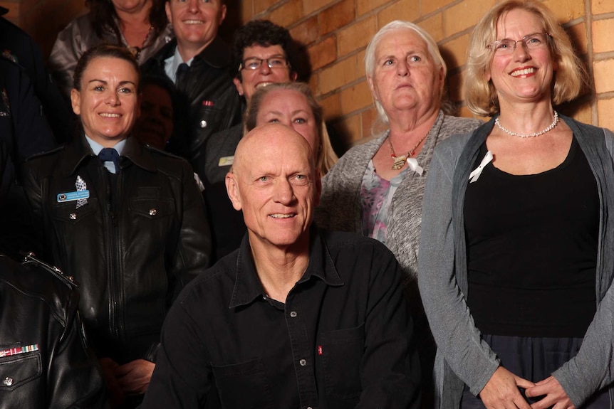 Musician and activist, Peter Garrett, in a black shirt sits in front of a group of people some in police uniforms
