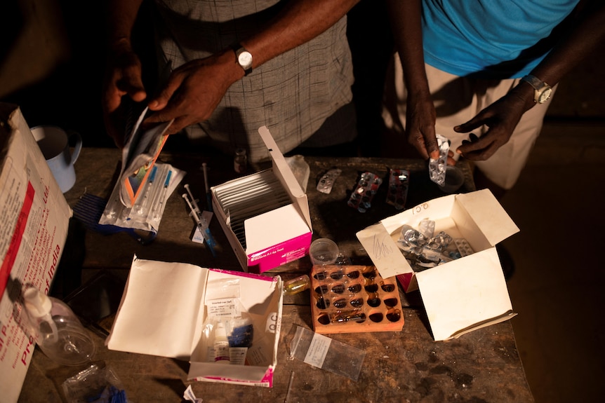 different types of medicines cover a table as two people sort through the medication