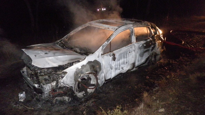 A burnt out car with a small flame