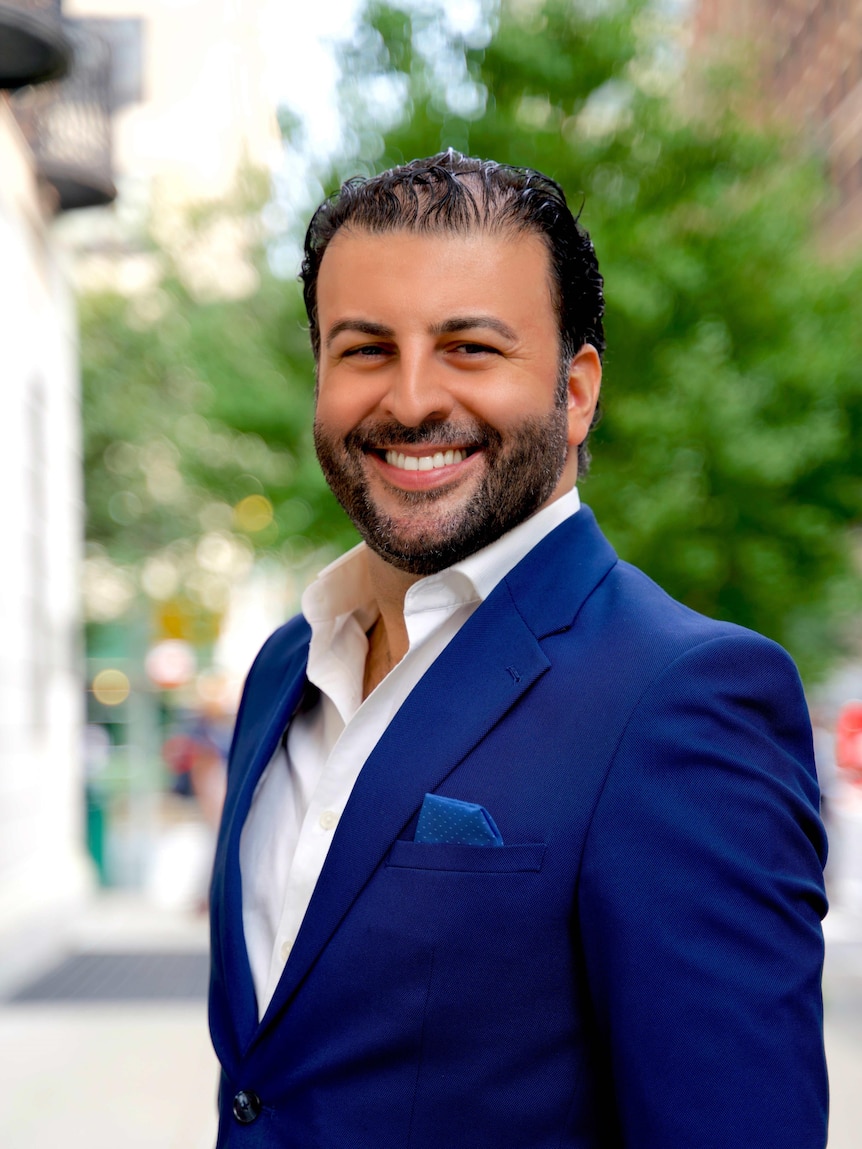 Opera singer David Serero smiles at the camera and wears a blue suit.