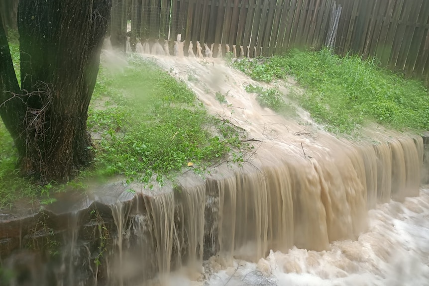 Water gushes through a fence and down a retaining wall.