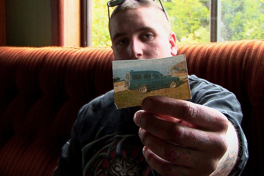 A young man holds a photo of his car