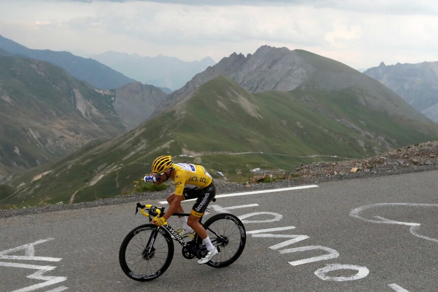 A cyclist wearing the yellow jersey takes a drink as he descends a mountain at the Tour de France.