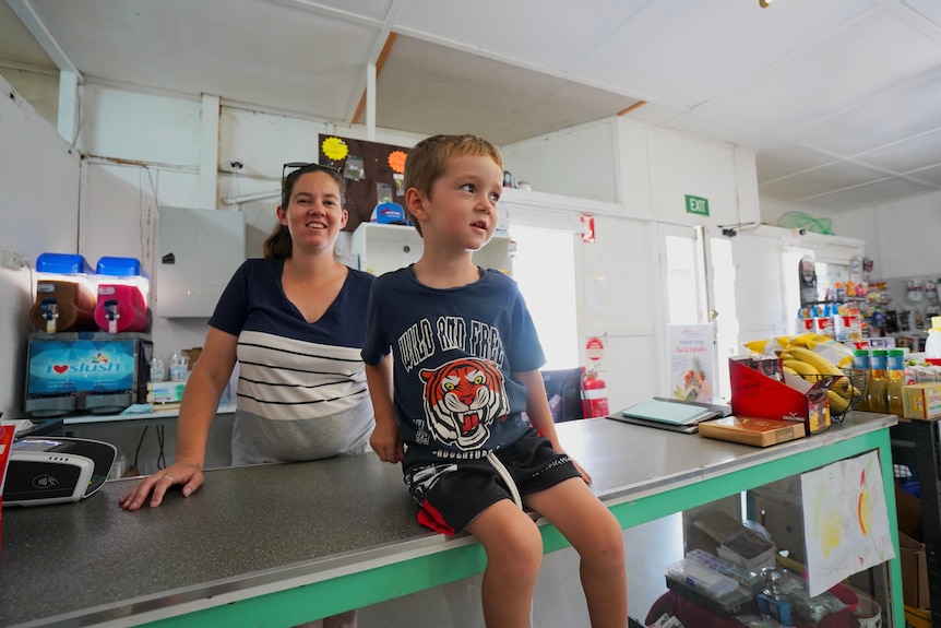 A three-year-old boy sits on the counter with his mum smiling behind him