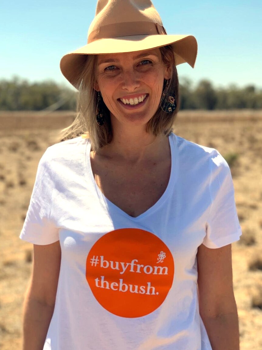 A woman stands in a paddock with a shirt reading #buyfromthebush.