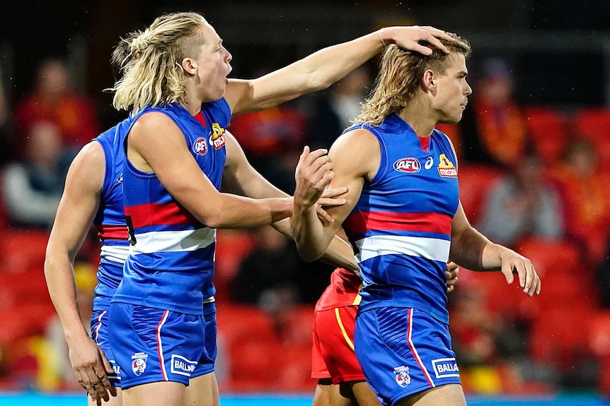 A Western Bulldogs AFL player pats the head of a teammate with his left hand as they celebrate a goal against Gold Coast Suns.