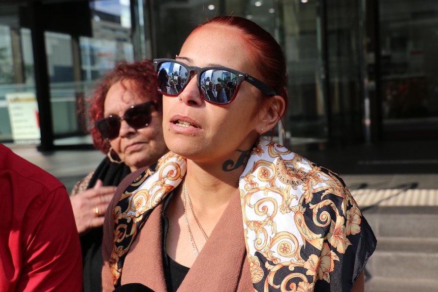 A woman wearing reflective sunglasses looks emotional outside court. 