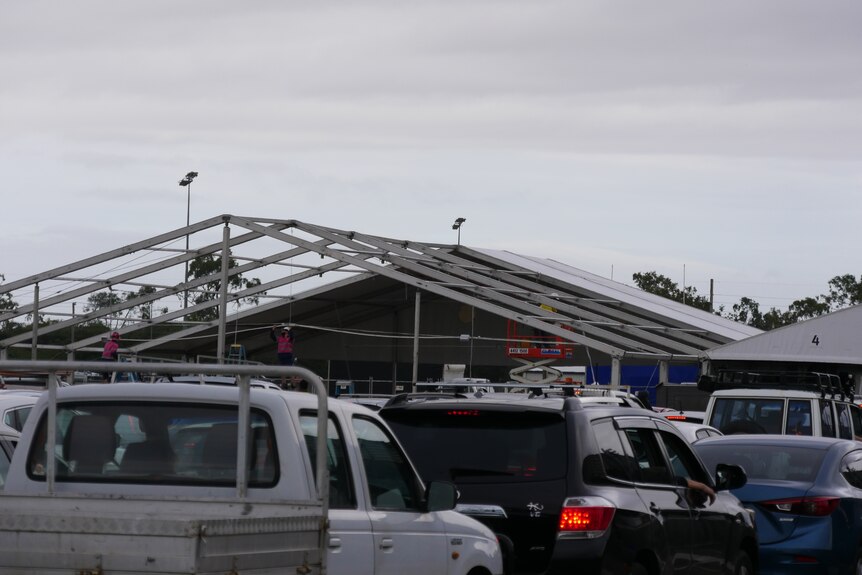 The steel shell of a roof being built with queue of cars in the foreground.