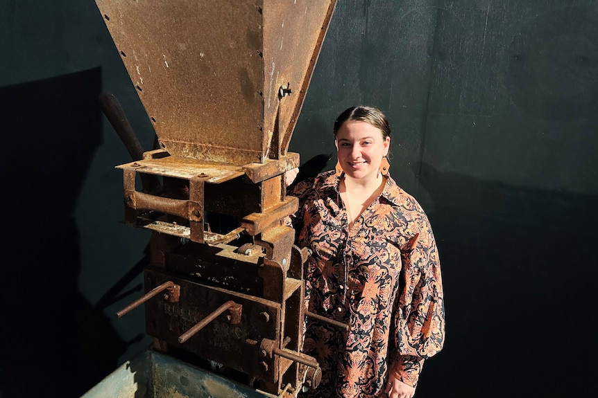 A smiling woman stands beside a tall metal contraption used to make bricks.