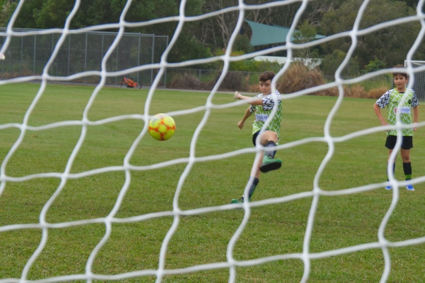 A young boy kicks a yellow soccer ball into a net