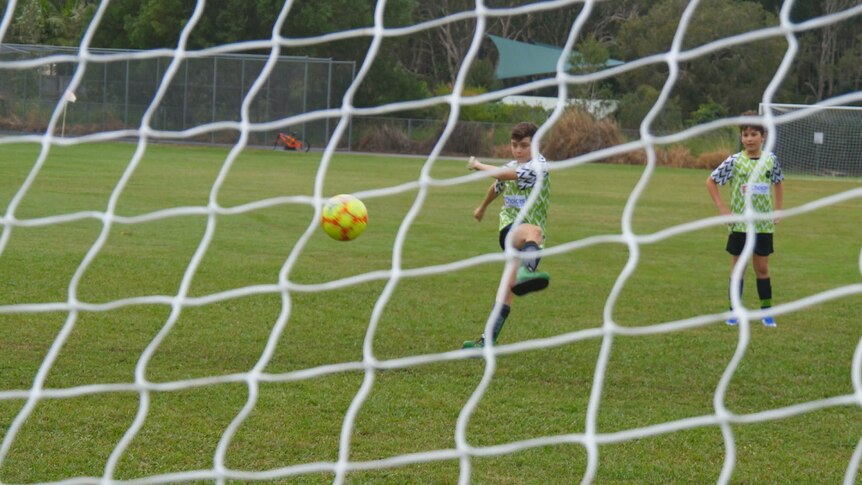 A young boy kicks a yellow soccer ball into a net