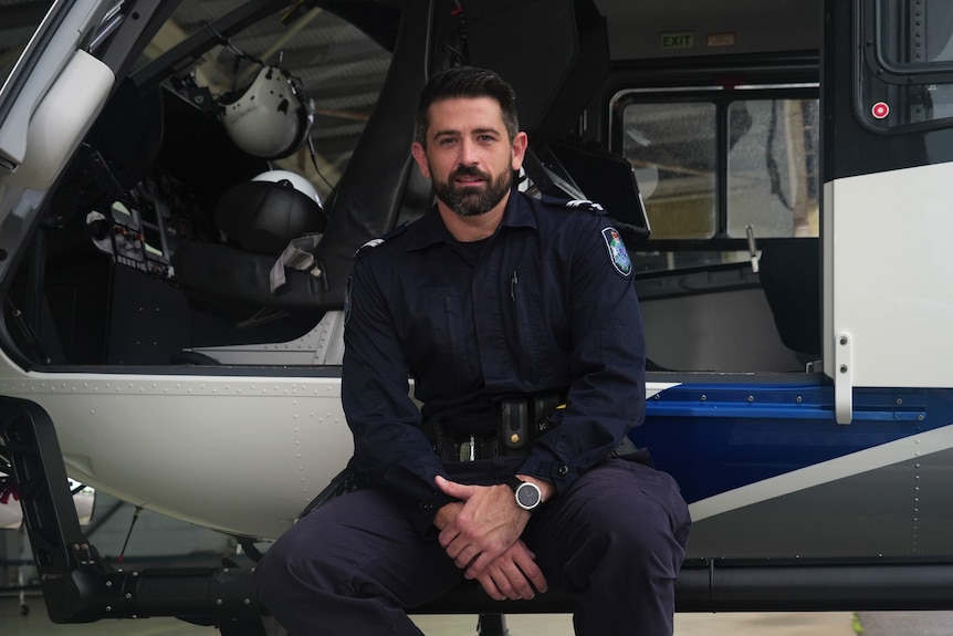 John Robinson in police uniform, in front of a QPS helicopter.