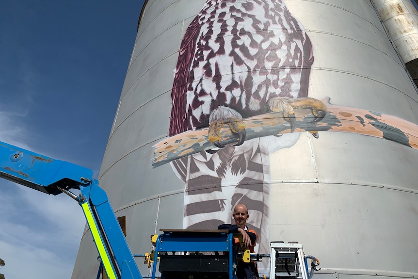 Artist with silo behind with painting of owl on it