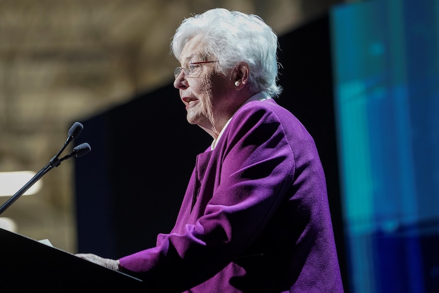 Alabama Governor Kay Ivey speaking at a lectern in a purple outfit