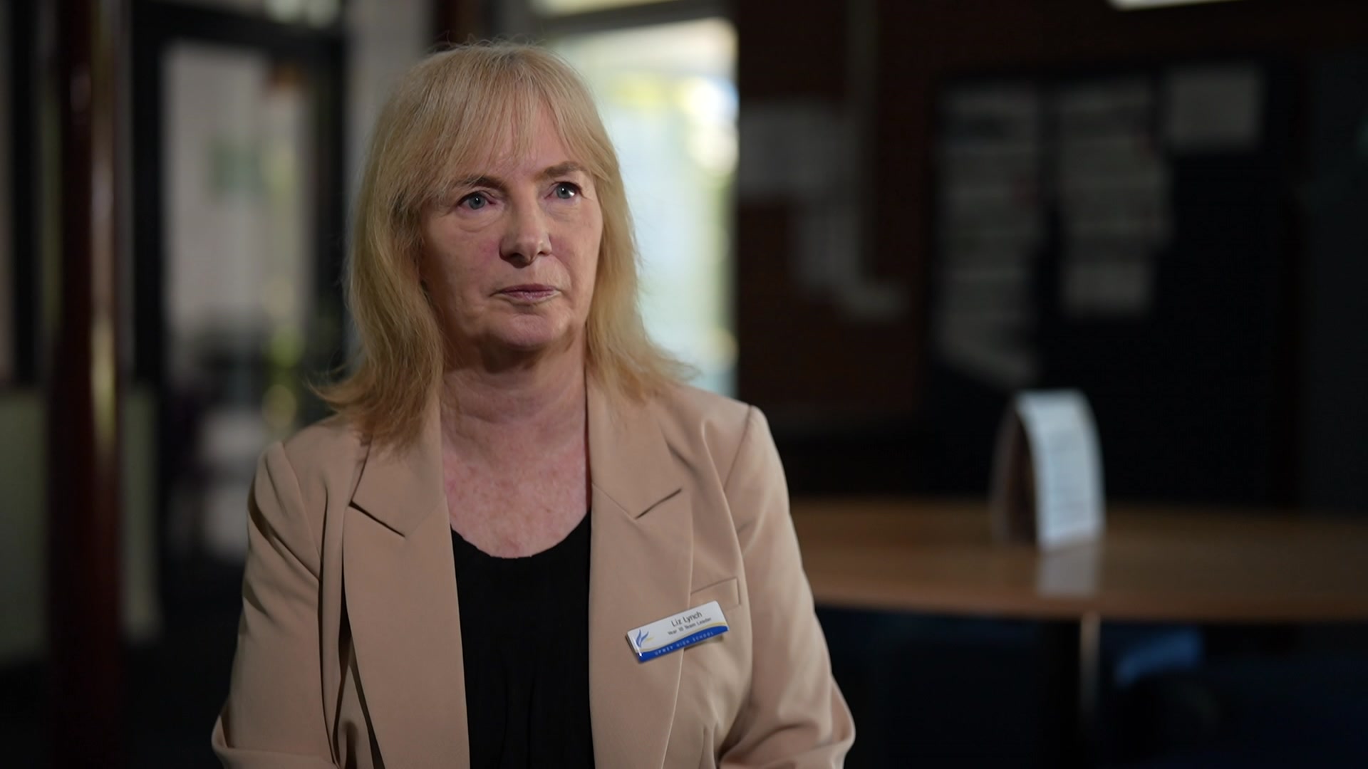 Mujer de cabello rubio y flequillo al frente, vestida con una chaqueta beige.