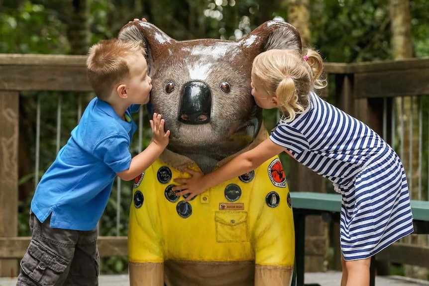 Two children hug Hello Koala sculpture Ranger Riley.