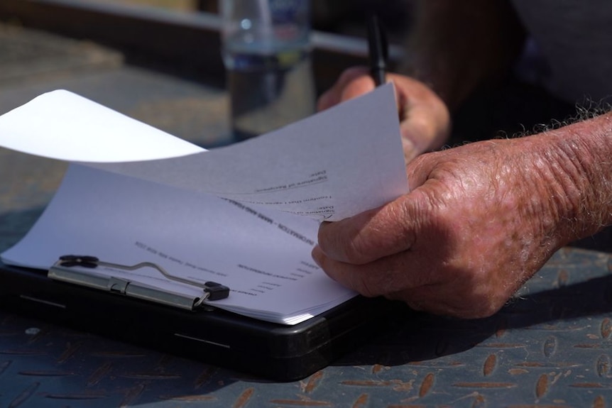 Close-up of a man's hands turning a page on a clipboard and signing with his other hand.