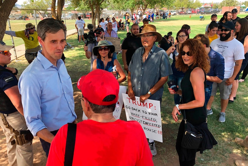 From a high angle, you look down at a crowd of people meeting Beto O'Rourke holding anti-Trump signs.