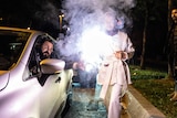 A woman lights a flare standing next to a car