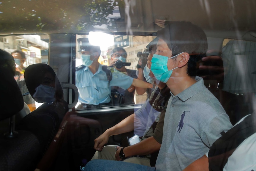 Pro-democracy legislator Ted Hui sits in a car with police wearing a face mask.