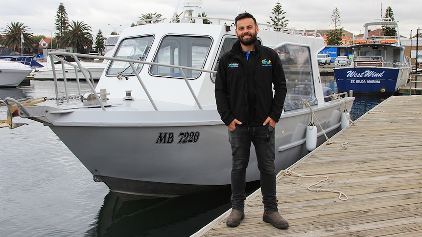OzFish senior project officer Ben Cleveland stands in front of a white fishing charter boat at St Kilda Marina.
