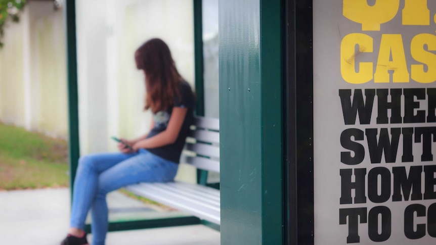 Anonymous person sits at a bus stop holding their phone