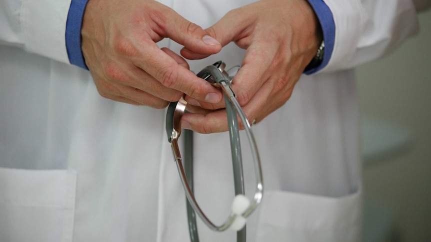 A doctor holds a stethoscope in two clasped hands