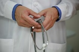 A doctor holds a stethoscope in two clasped hands.