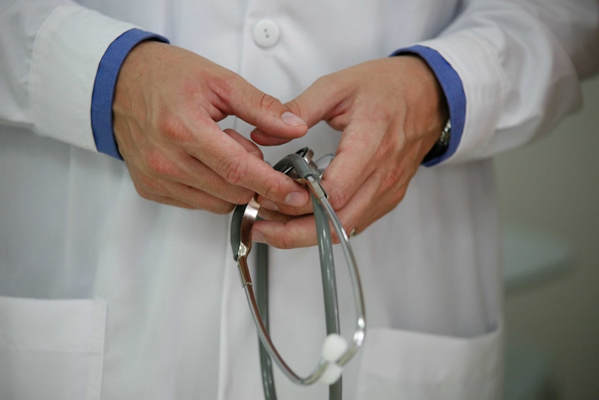 A doctor holds a stethoscope in two clasped hands