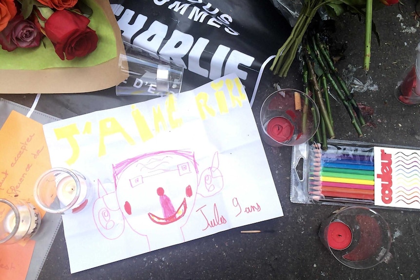 A child's drawing among flowers and candles in a roadside tribute