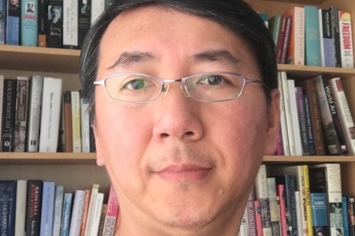 A photo of a man with glasses with bookcases in the background. 