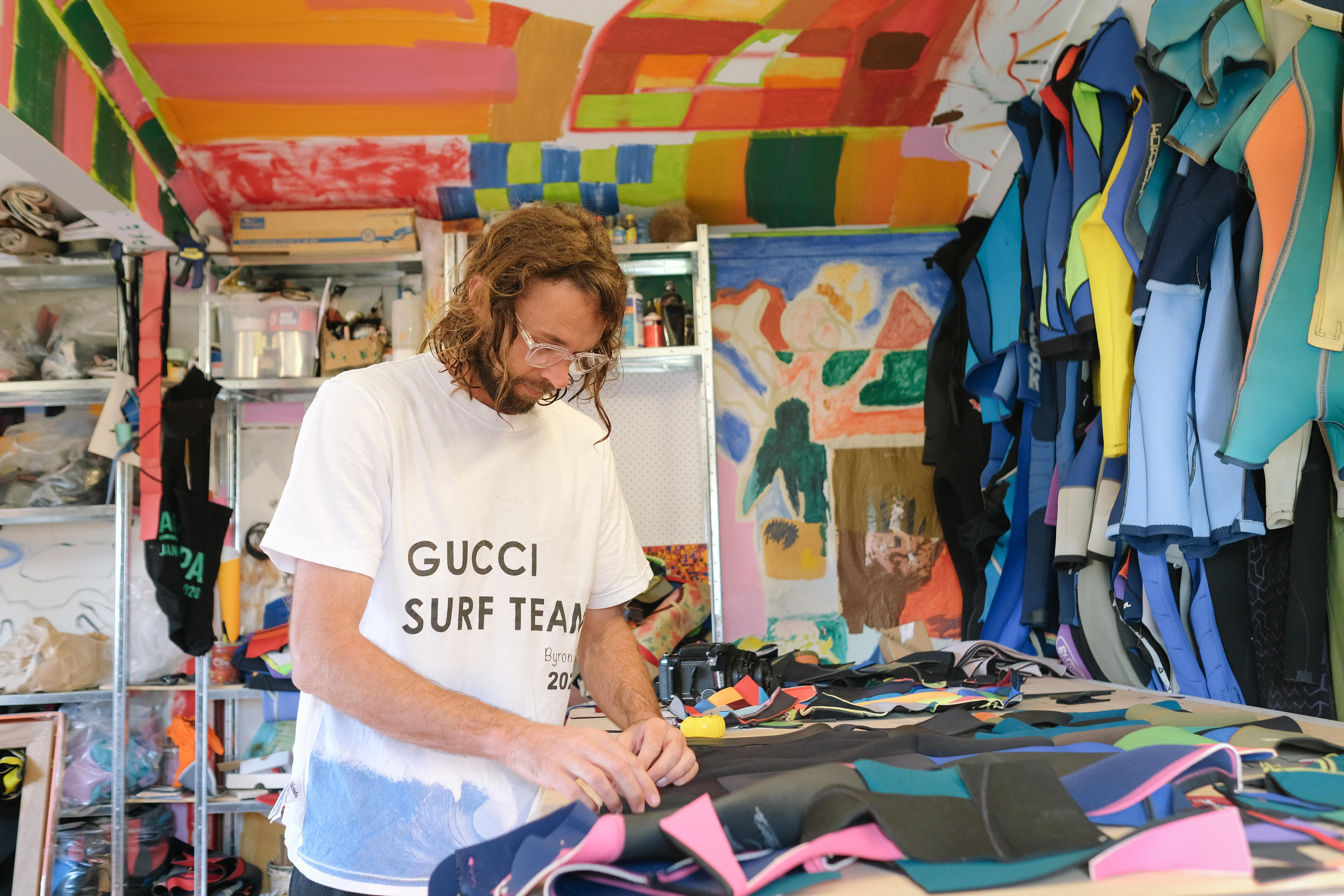 Artist works in his colourful studio. Standing at a table curring and arranging neoprene wetsuit material 