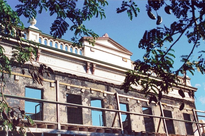 Blackened parts of a heritage building, glass-less window frames and construction scaffolding stand against a blue sky