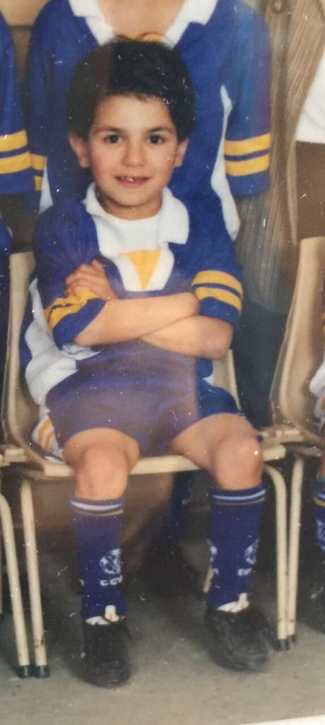 A young boy wearing blue, white and yellow soccer clothes poses for a photo