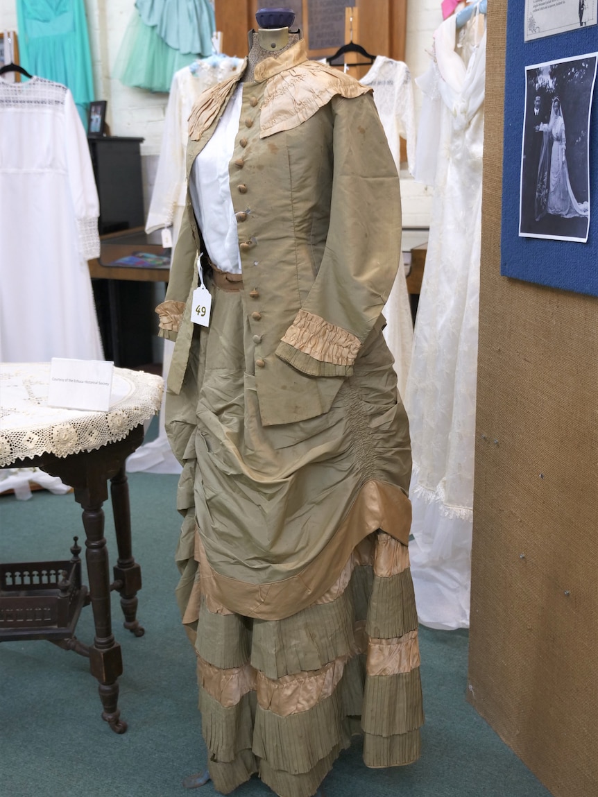 A button up top in a tan colour has a lighter, ruffled collar and a floor length skirt with gathered frills. 