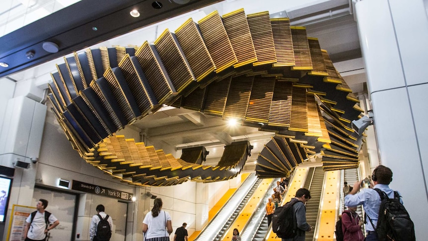 The Interloop sculpture suspended from the ceiling above the base of a set of escalators.