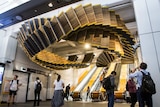 The Interloop sculpture suspended from the ceiling above the base of a set of escalators.