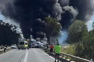 Black smoke plumes over a crash on the road with cars backed up.