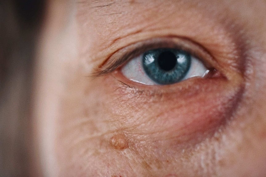 A still from Hoda Afshar's video work Agonistes, a close up shot of a white wrinkled skin and a blue eye